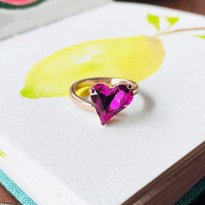 heart shaped ring with pink swarovski - this is an adjustable ring. places against a coloured backdrop. 