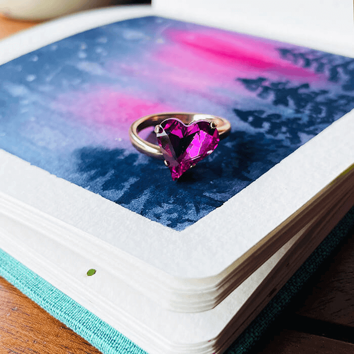 heart shaped ring with pink Swarovski - this is an adjustable ring. On coloured background to show complexity of colour. 